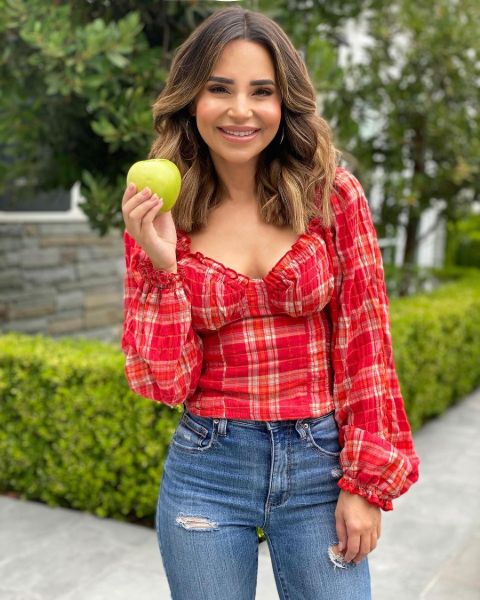 Rosanna Pansino in a red shirt eating a fruit.